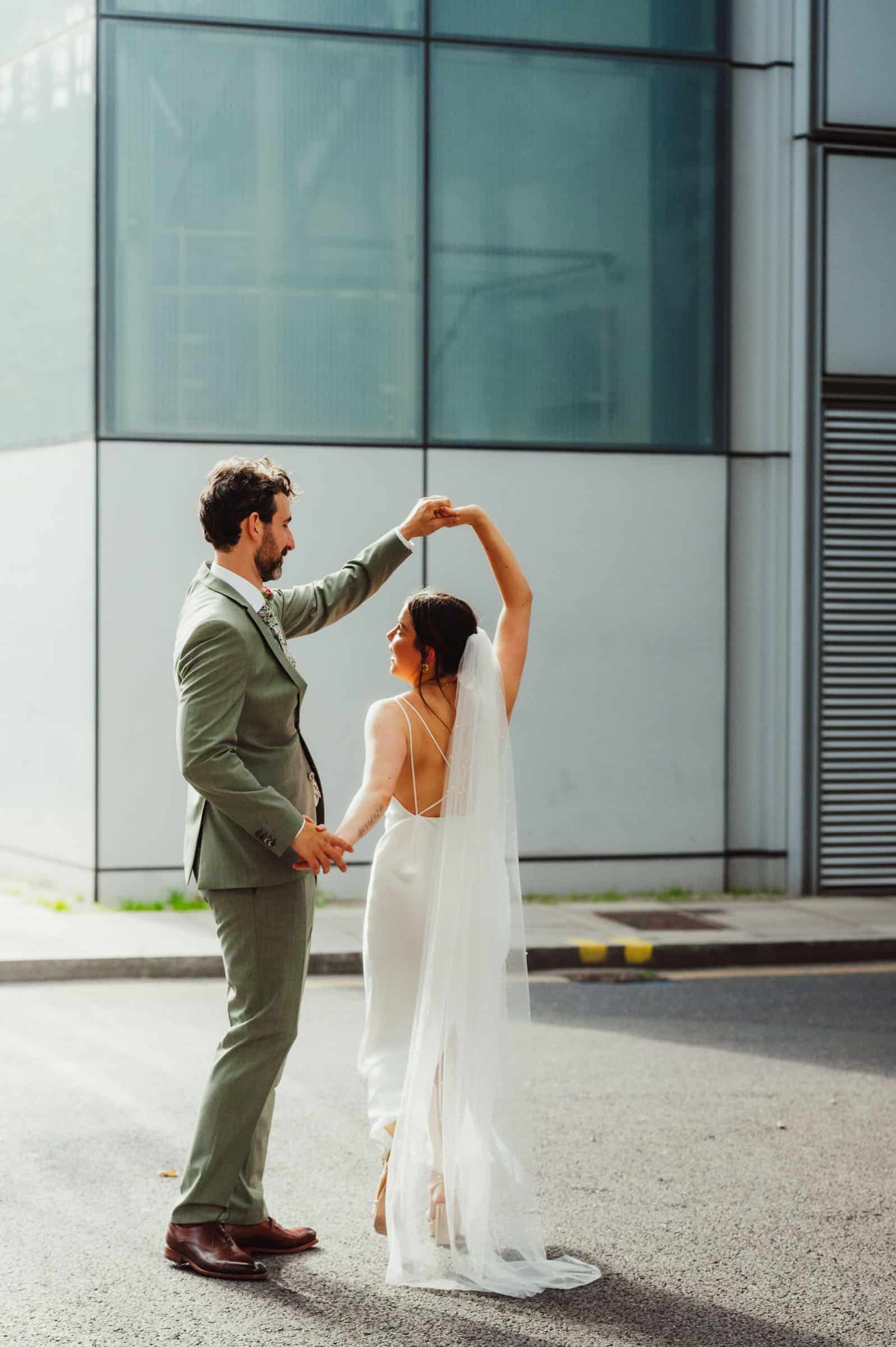 Stylish couple standing outside cinema with marquee sign, bride in blue floral dress with heart sunglasses, creative London wedding portrait