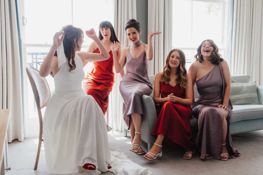 Bridesmaids in colourful dresses sharing laughter and joy at wedding prep.