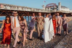 Diverse wedding party in colourful attire celebrating at Brighton Palace Pier, backdrop of the iconic seaside pier.