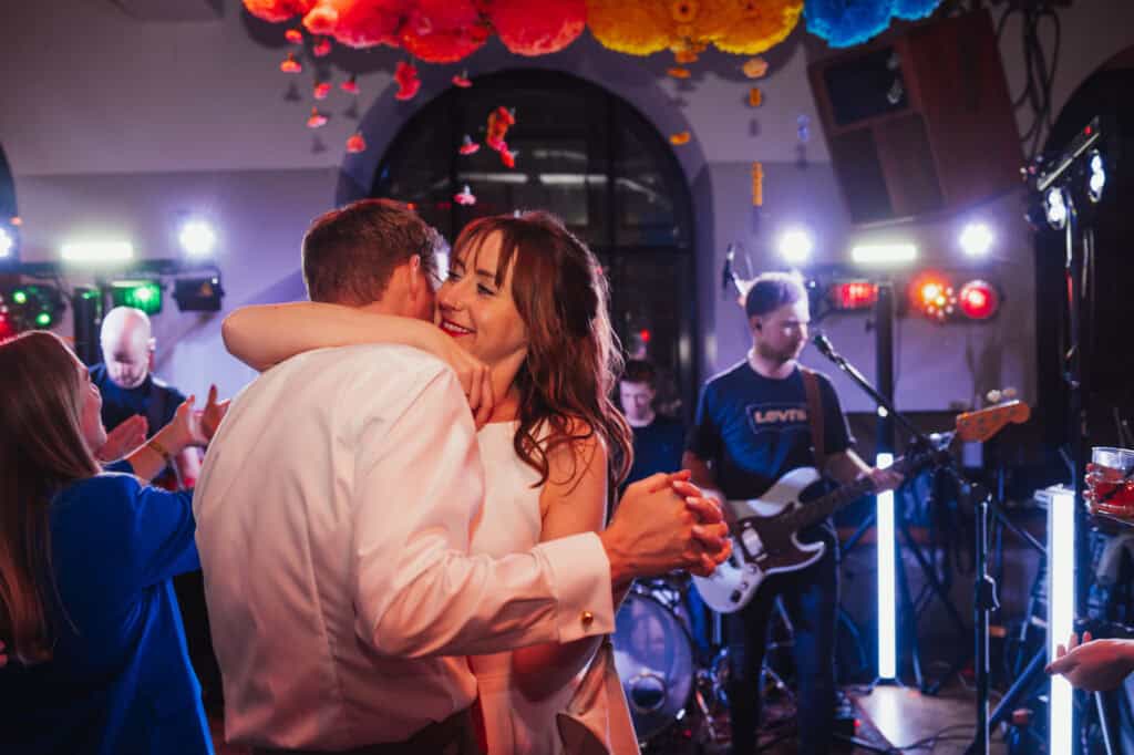 An energetic couple dancing closely at a lively music gig, surrounded by enthusiastic guests and live band.
