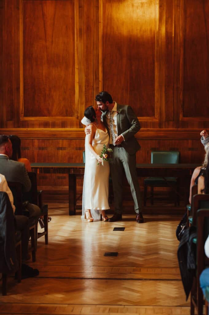 Beautiful couple kissing at wedding ceremony with wooden panel background.
