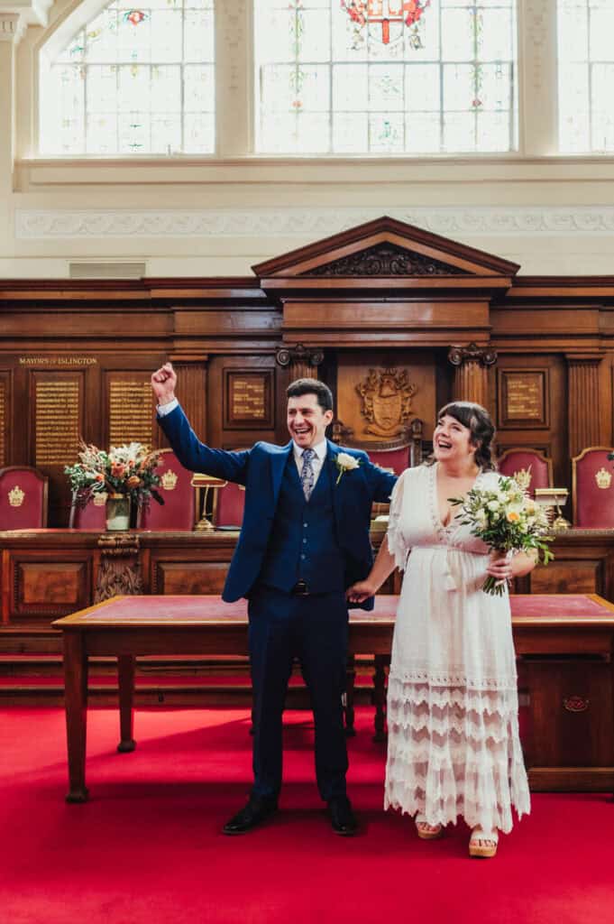 Happy couple celebrating their wedding in a historic town hall with wooden interior and stained glass windows.