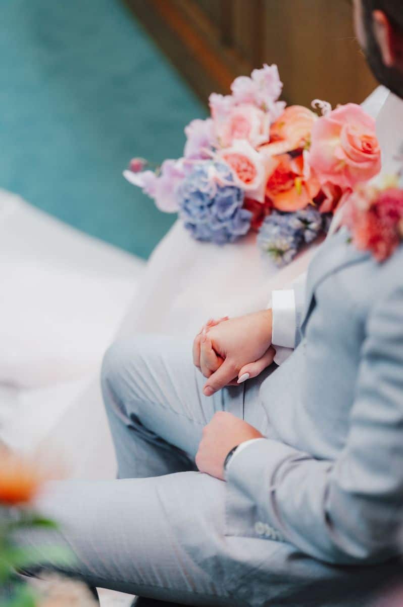 Close-up of couple holding hands with colourful bouquet during ceremony at Camden Town Hall, by Sidey Clark