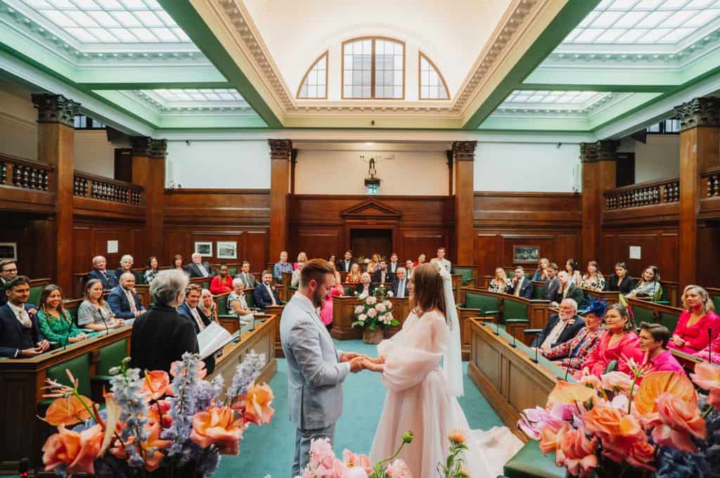 Wide view of wedding ceremony at Camden Town Hall with colourful floral arrangements, photographed by Sidey Clark