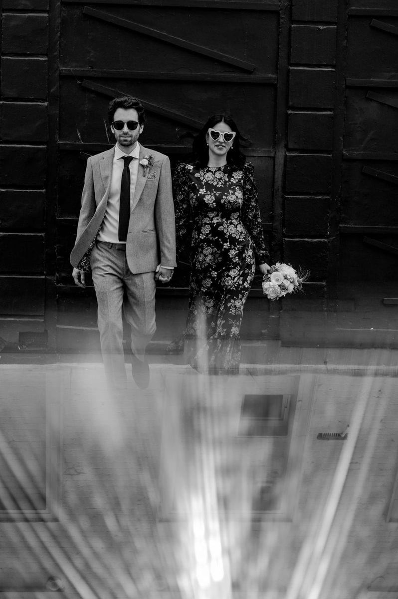 Stylish couple in heart sunglasses and floral dress standing together in black and white, London wedding by Sidey Clark