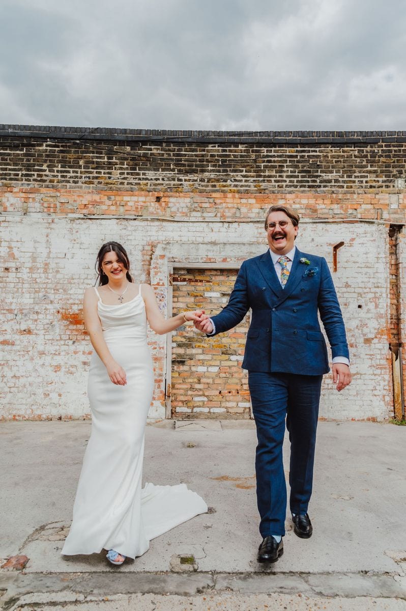 Bride and groom laughing and holding hands at an industrial London wedding venue, by Sidey Clark