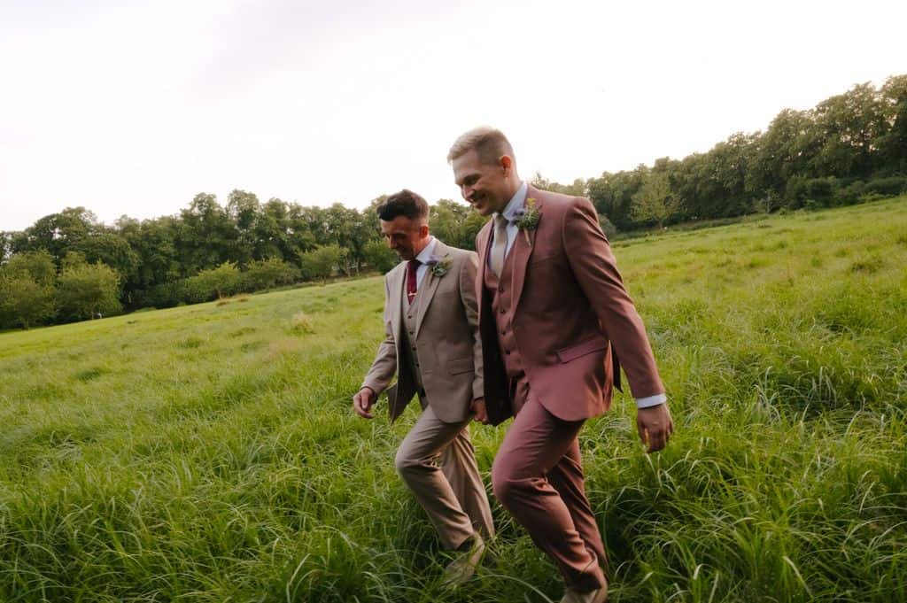 Two grooms walking hand in hand through meadow