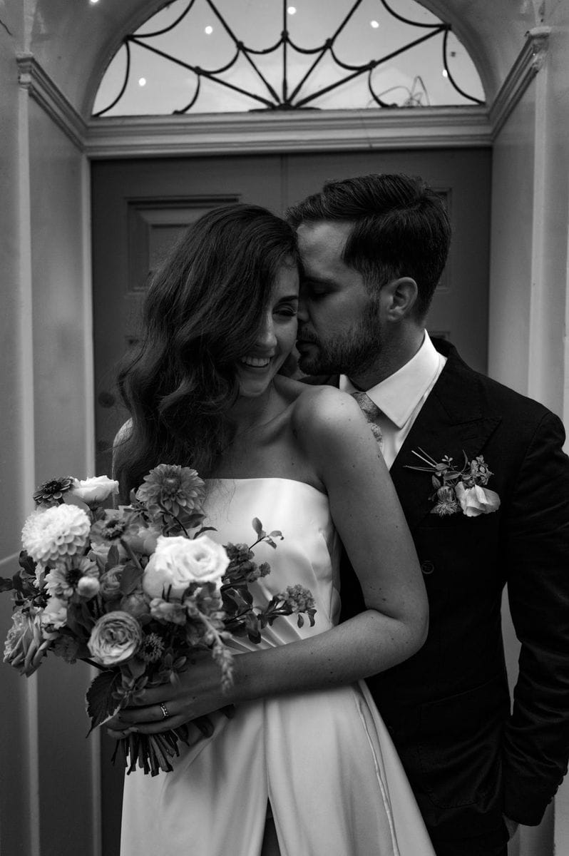 Black and white portrait of bride and groom embracing with bouquet at Pelham House autumn wedding by Sidey Clark